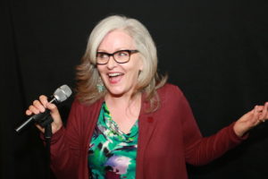Tracy DeGraaf, breast cancer survivor and comedian, laughing into a microphone